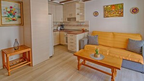 Kompakti oleskelutila, jossa on pieni keittiönurkkaus, sohva ja ruokapöytä.