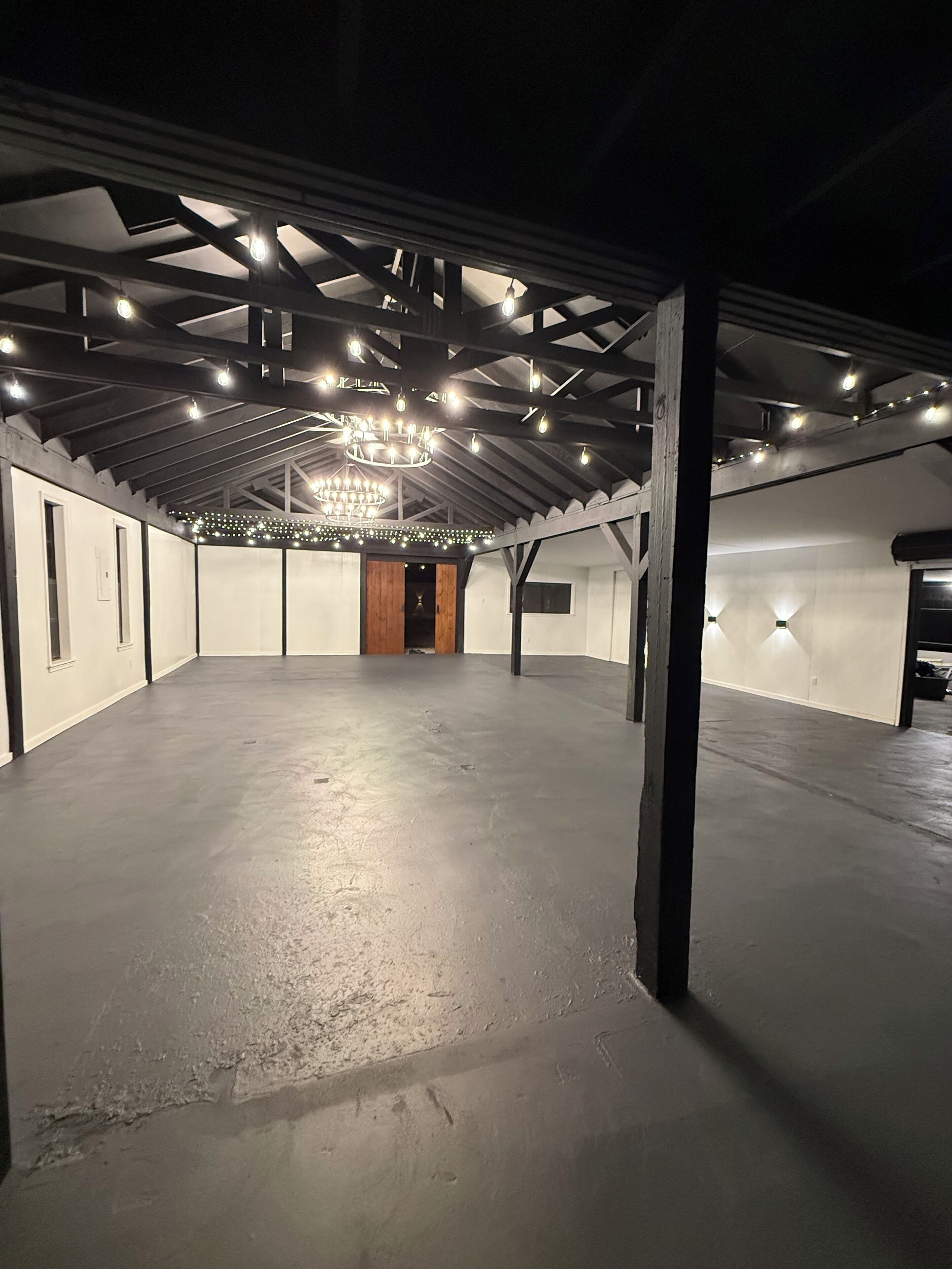 An indoor space with a high ceiling, exposed beams, and a central chandelier.