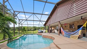 A covered outdoor swimming pool with a view of the surrounding landscape, a brick building with a sign, and outdoor seating. - Ranch with pool/Lake fishing kayak Paddleboard Soccer Motocross 30 min to Disney (Clermont)