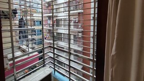A view through a window with metal bars, revealing a multi-story building with balconies and a brick facade. - Nicely 3 bedrooms apartment at Mohammadpur (Dhaka)