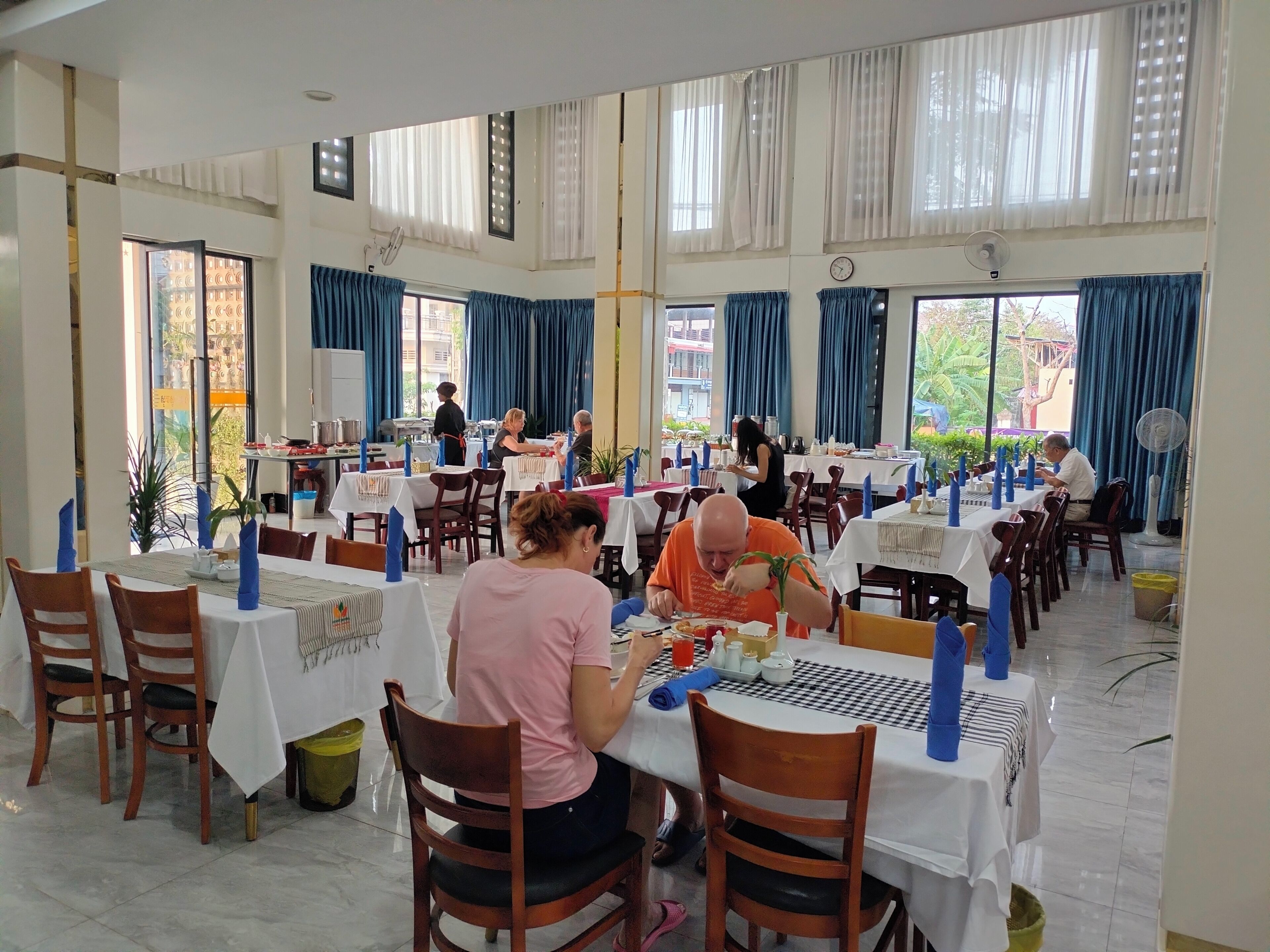 A restaurant with multiple tables and chairs, large windows with curtains, and a clean, tiled floor.