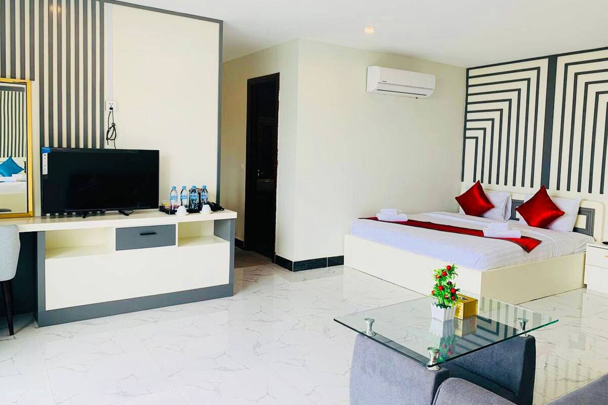 A modern hotel room with a bed, a TV, a desk, and a glass coffee table.