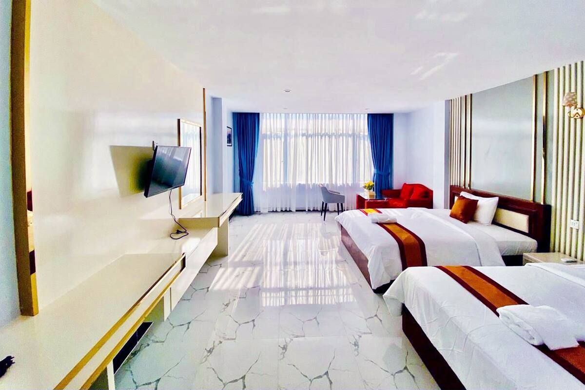 A hotel room with two beds, a desk, a chair, a TV, and a window with curtains.