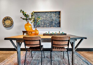 Ein Essbereich mit einem Holztisch, zwei Ledersesseln, einer Blumenvase und einem Wanddekor.