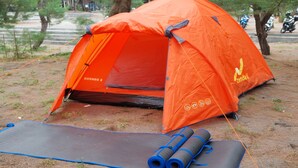 Une tente orange avec un tapis bleu et des tapis enroulés à proximité.