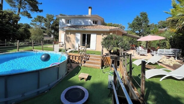 Uma casa com piscina, trampolim e área de estar no pátio com móveis de exterior.