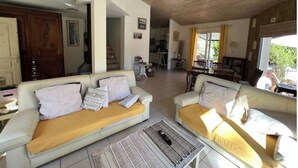 Uma sala de estar ampla, com dois sofás, uma mesa de centro e uma cozinha ao fundo.