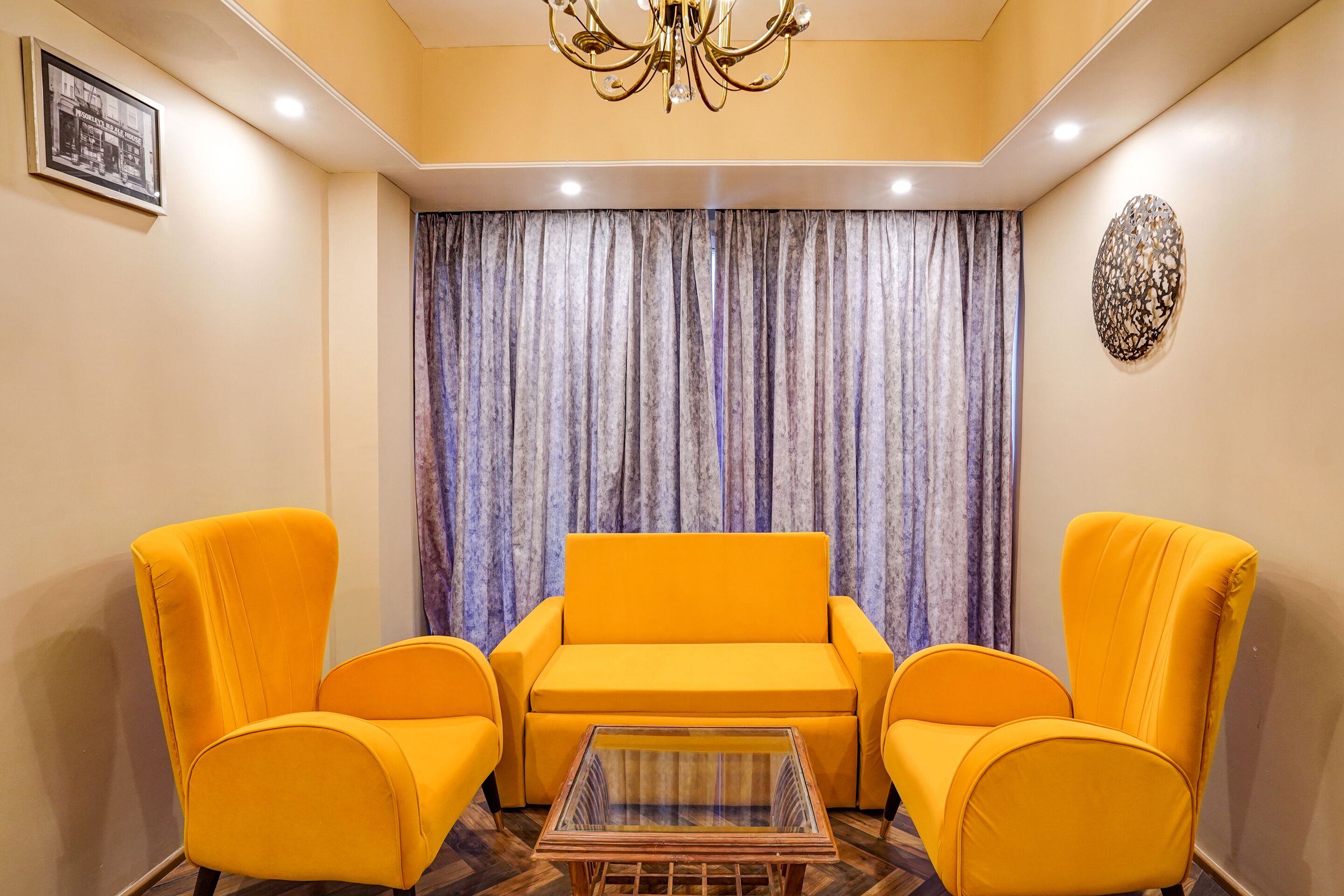 Una habitación con un sofá amarillo, una mesa de centro de vidrio y una lámpara de araña.