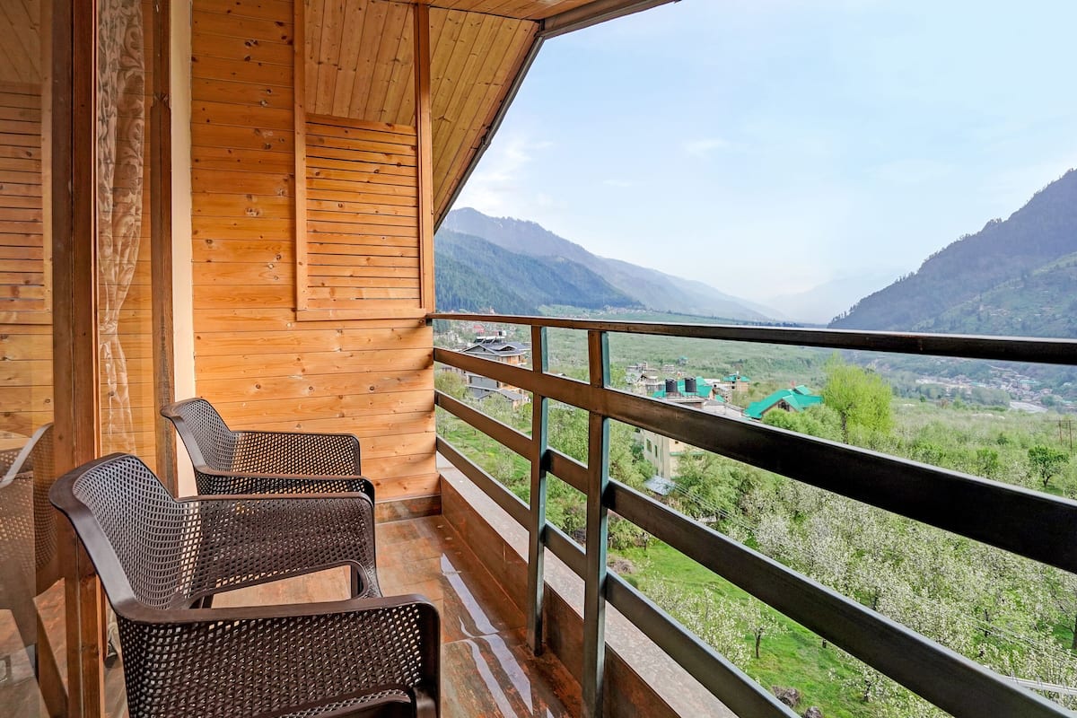 Un balcón de madera con sillas de mimbre, con vistas a un valle y montañas.