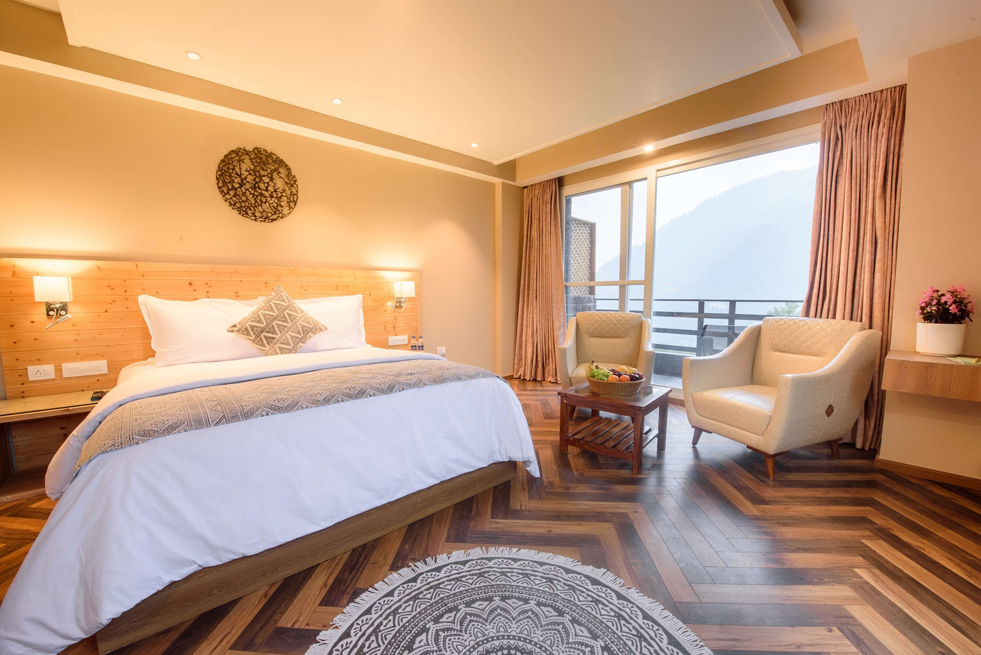 Camera d'albergo con un letto grande, una sedia, un tavolino e vista sulle montagne dalla finestra.
