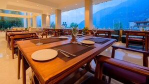 A restaurant with wooden tables, white plates, and wine glasses, set against a backdrop of mountains. - Naturevilas Sarovar Premiere Manali (Manali)