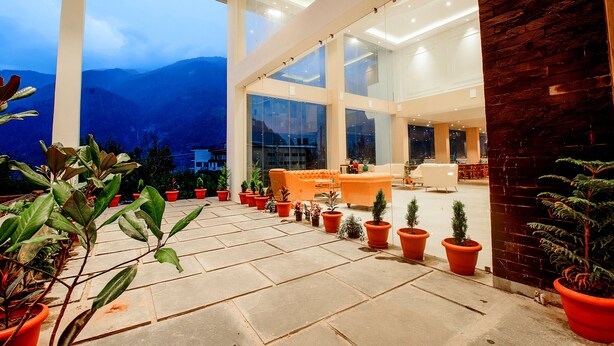 A spacious indoor area with large windows, potted plants, and a seating area. - Naturevilas Sarovar Premiere Manali (Manali)