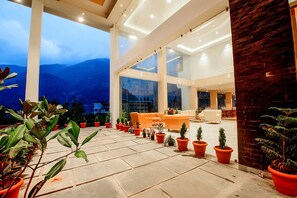 A spacious indoor area with large windows, potted plants, and a seating area. - Naturevilas Sarovar Premiere Manali (Manali)