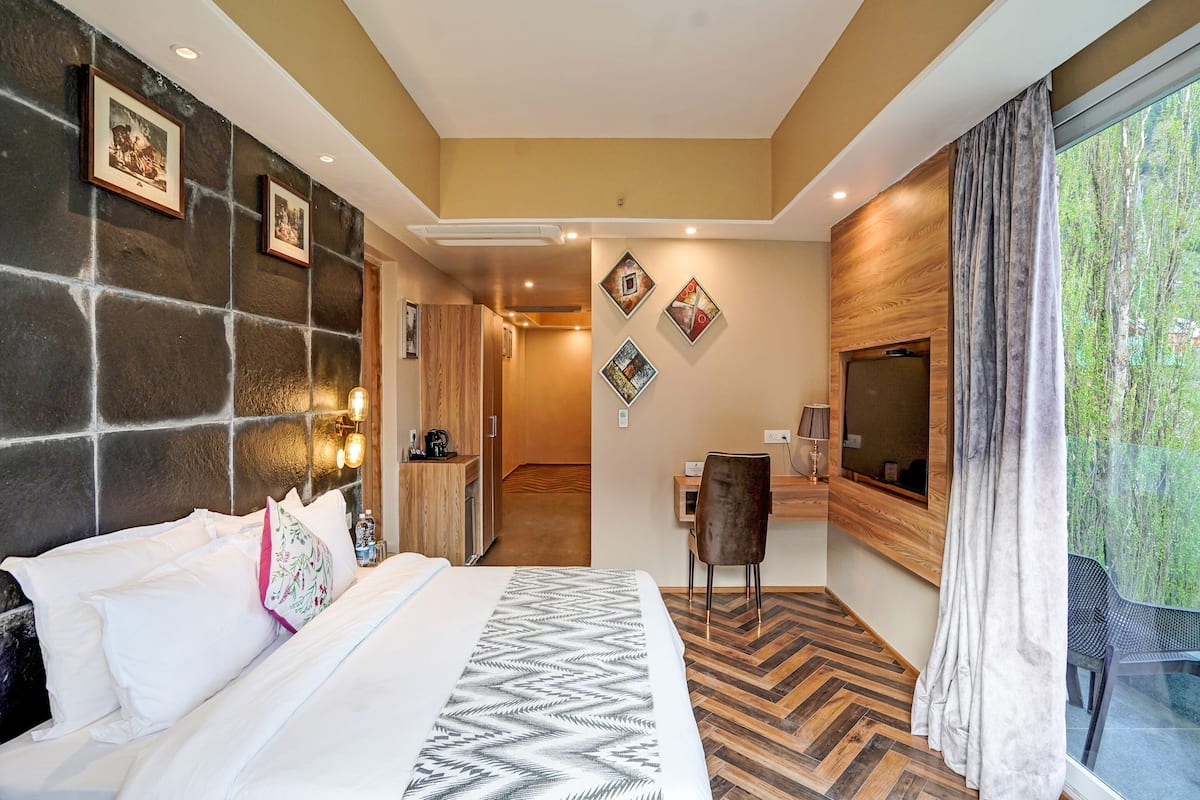 Habitación de hotel con una cama grande, un escritorio, una silla y vistas a zonas verdes a través de la ventana.