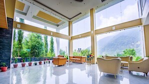 A spacious lobby with large windows, a modern ceiling design, and a variety of seating arrangements. - Naturevilas Sarovar Premiere Manali (Manali)