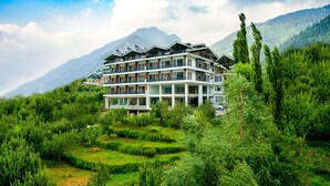 A multi-story hotel with a modern architectural design, situated in a lush green valley with terraced fields and a mountain backdrop. - Naturevilas Sarovar Premiere Manali (Manali)