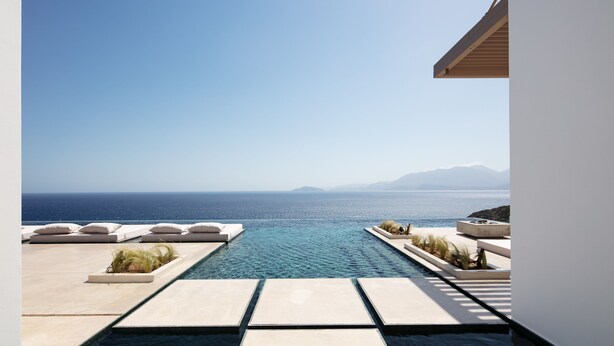 Une piscine à débordement moderne offrant une vue dégagée sur la mer et les montagnes lointaines.