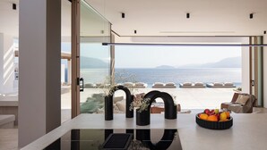 Une cuisine moderne dotée d’un grand îlot central, offrant une vue sur la mer, et d’un espace détente avec des meubles d’extérieur.
