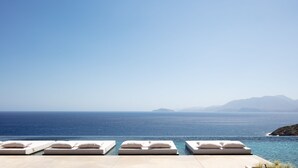 Un espace aménagé au bord de la piscine, avec des chaises longues et une vue sur la mer et les montagnes lointaines.