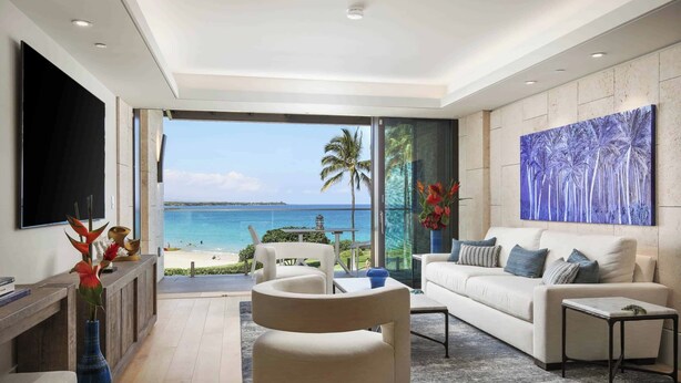 Sala de estar moderna com uma televisão grande, assentos confortáveis, vista para a praia e uma pintura com tema tropical.