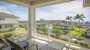 Un espace extérieur abrité, doté d’une table et de chaises, qui offre une vue sur un quartier résidentiel avec ses maisons et ses palmiers.