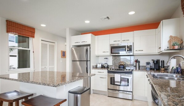 A modern kitchen with white cabinets, stainless steel appliances, granite countertops, and a central island with bar stools.