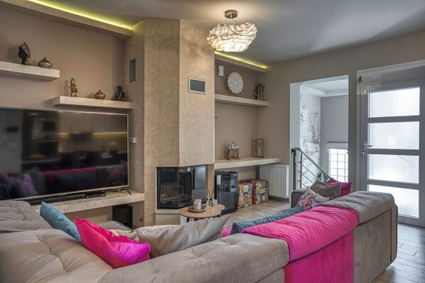 A living room with a large flat-screen TV, a fireplace, a sofa, and a staircase leading to another level.