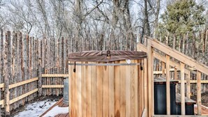 A wooden sauna structure with a metal roof, surrounded by a wooden deck and a wooden fence.
