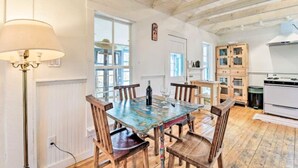 A dining area with a wooden table and chairs, a lamp, and a kitchen in the background.