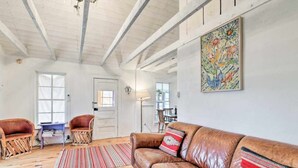 A spacious living room with a leather sofa, two wicker chairs, a patterned rug, and a painting on the wall.