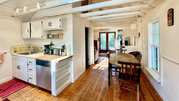 A spacious kitchen with a wooden dining table and chairs, a built-in dishwasher, and a red rug on the floor.