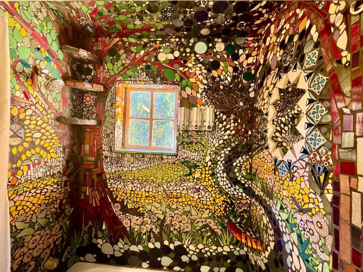 Une pièce avec un mur décoré de mosaïques, une fenêtre et une petite étagère.