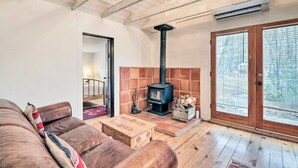 A cozy living room with a brown leather sofa, a wooden coffee table, a fireplace with a black chimney, and a large sliding glass door to the outdoors.
