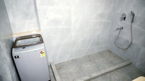 Un baño pequeño con lavadora blanca, ducha con cabezal de ducha manual y suelo de baldosas.