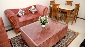 Una sala de estar con un sofá rojo, una mesa de centro de vidrio y una mesa de comedor de madera con sillas.
