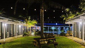 A nighttime outdoor area with a wooden picnic table, palm trees, and a building with a blue-lit entrance. - Mallacoota Hotel Motel (Mallacoota)