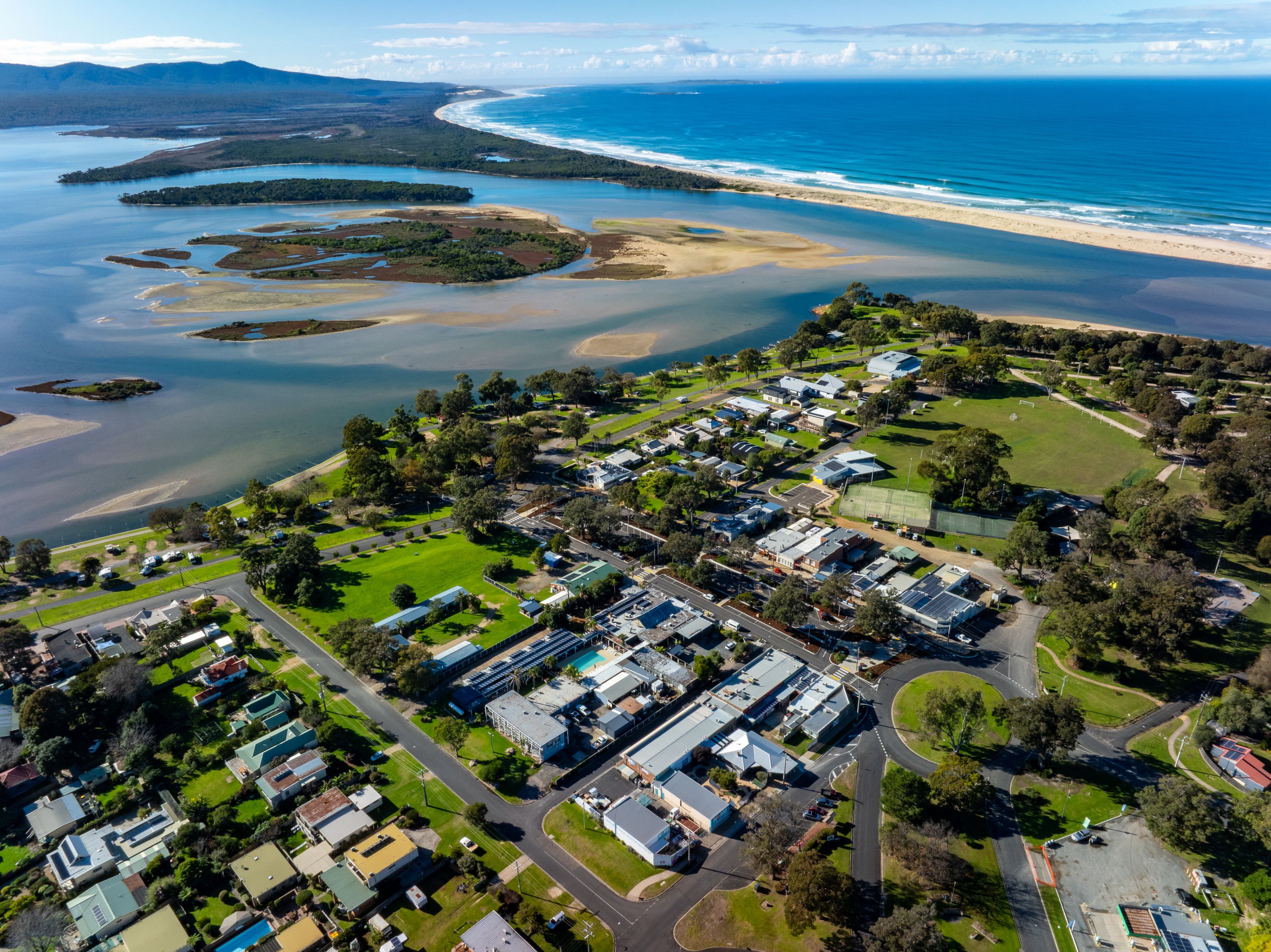 An aerial view of a coastal residential area with houses, roads, and a beach.