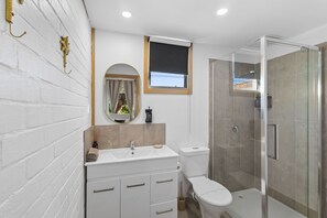 A modern bathroom with a white vanity, a toilet, a shower enclosure, and a window. - Mallacoota Hotel Motel (Mallacoota)