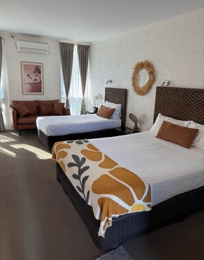 Une chambre d’hôtel avec deux lits, un canapé, un miroir et un climatiseur fixé au mur.