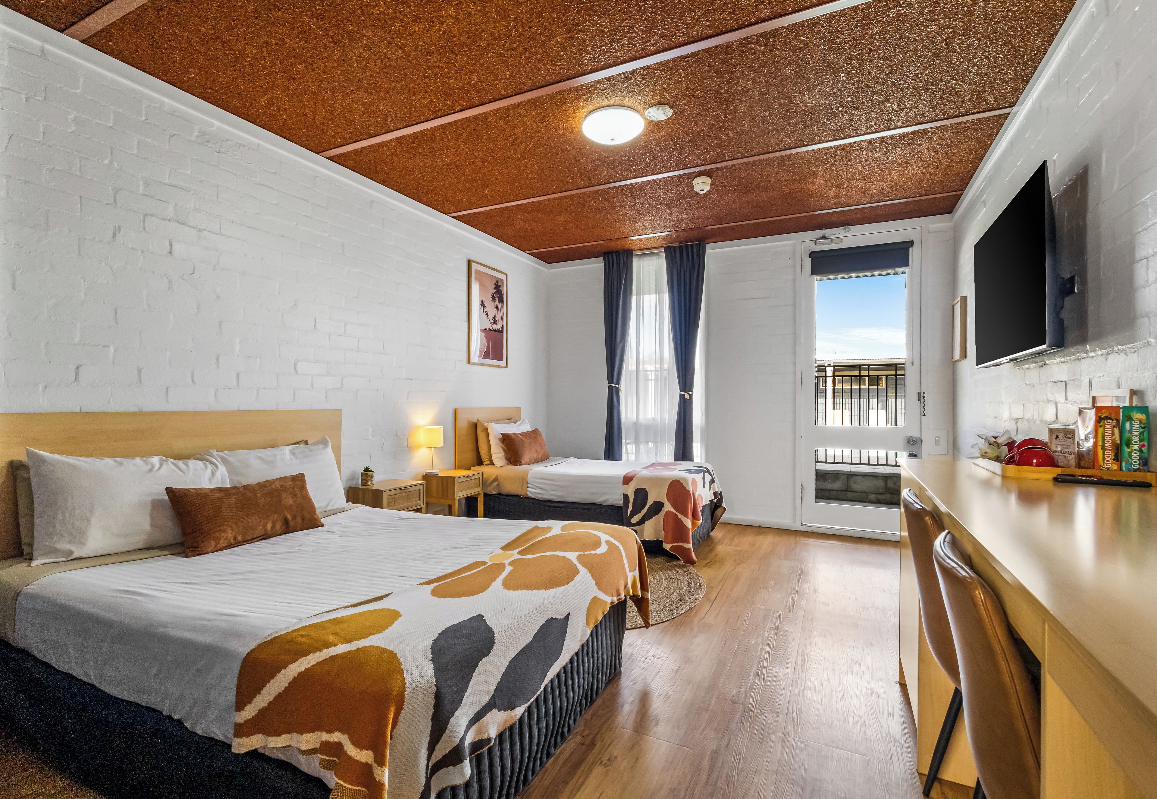 Ein Hotelzimmer mit zwei Betten, einem Fernseher, einem Schreibtisch und Blick ins Freie.