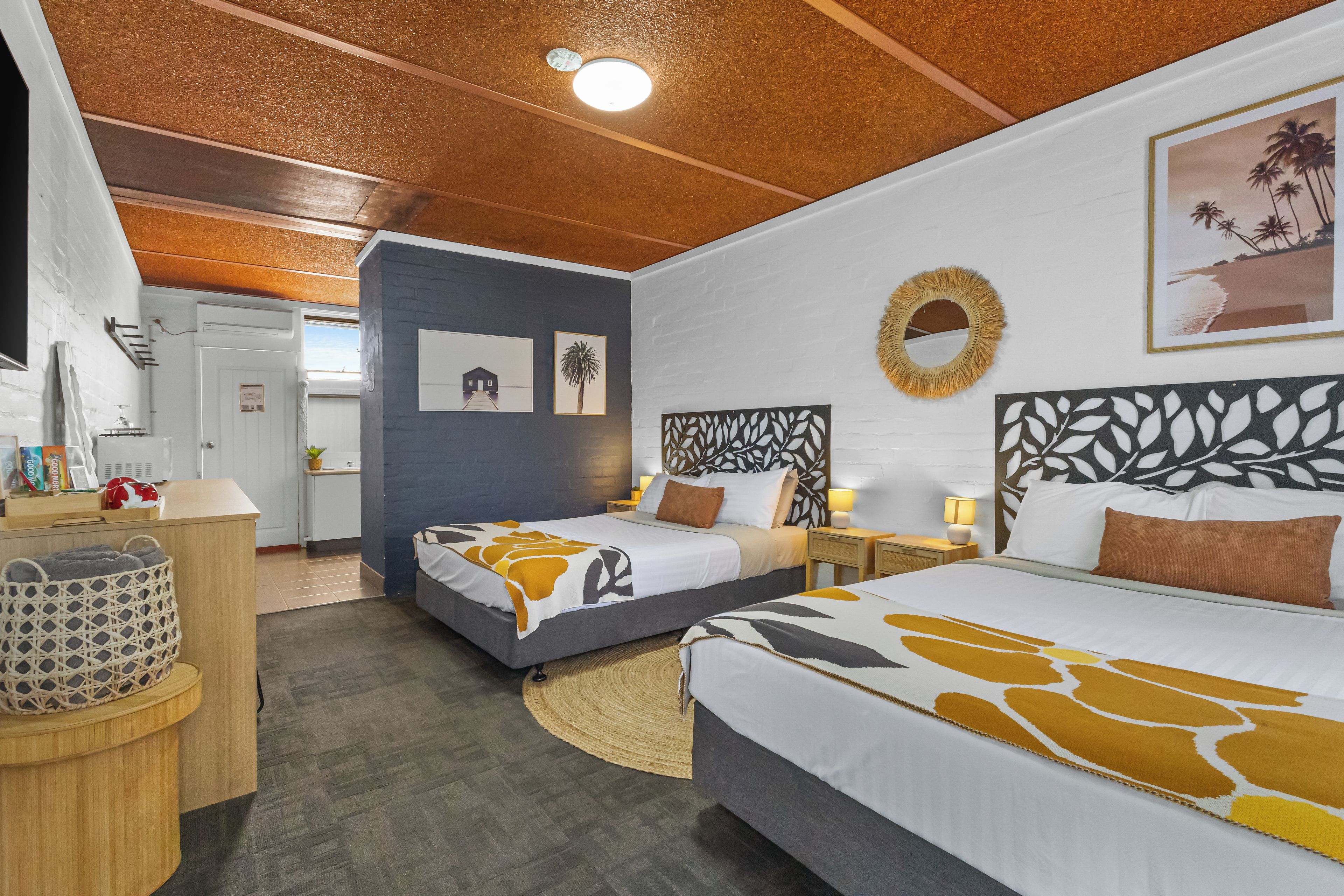 Ein Hotelzimmer mit zwei Betten, einem runden Spiegel und einem Gemälde mit Strandmotiv.