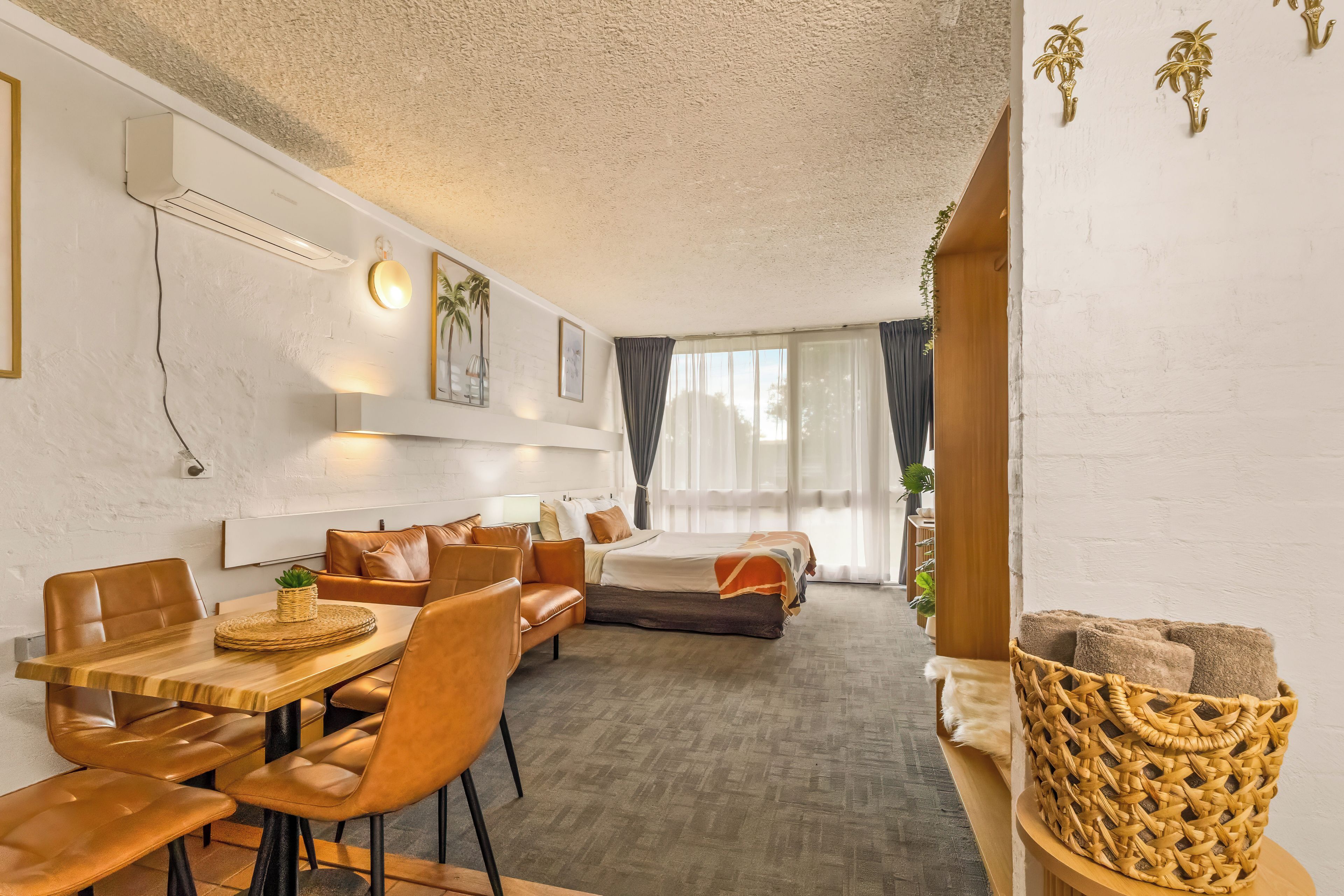 A hotel room with a dining area, a sofa, a bed, and a large window with curtains.
