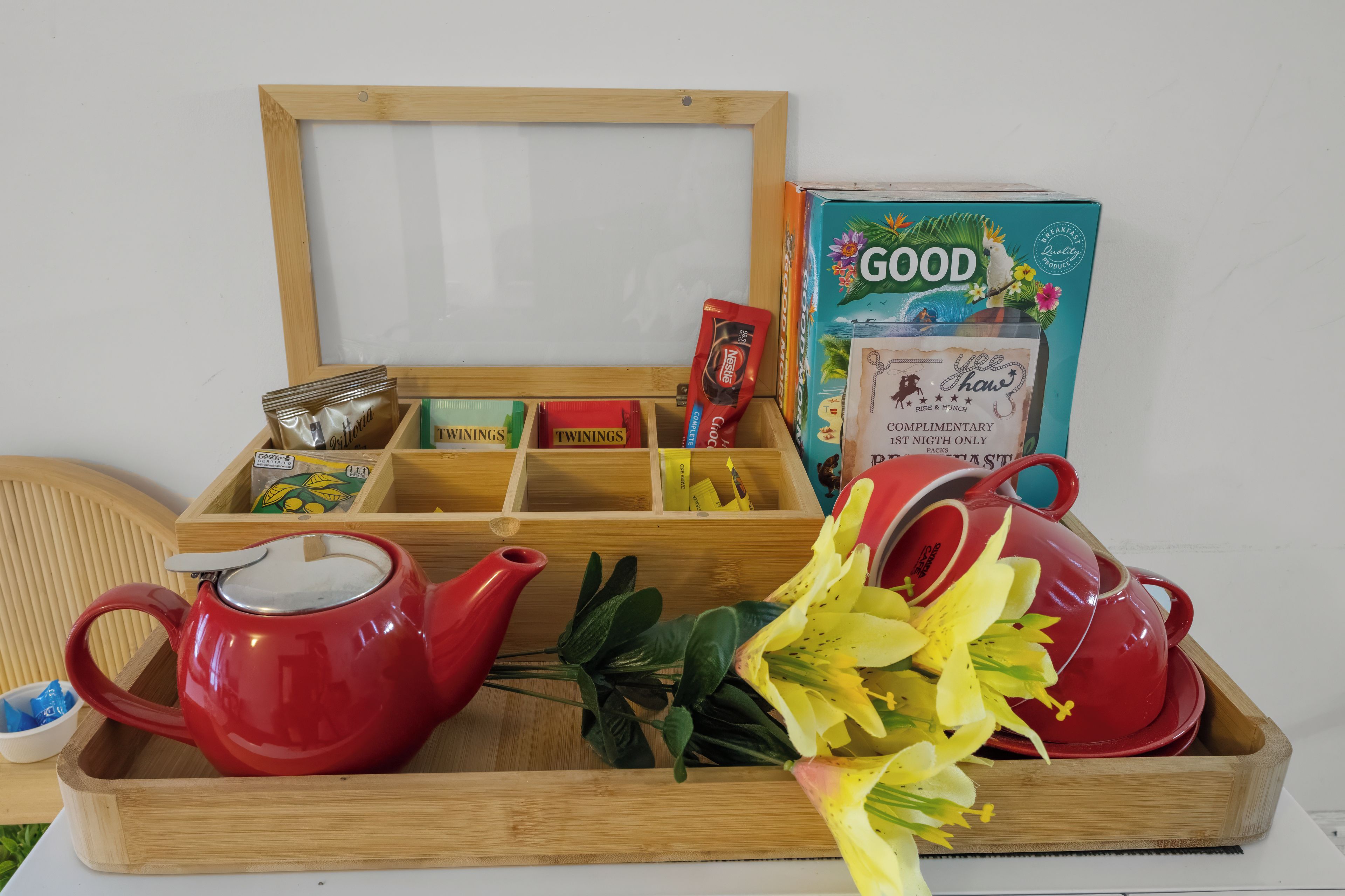Una bandeja de madera con una tetera roja, una taza roja, una caja de Good Oats y una caja de té Twinings.