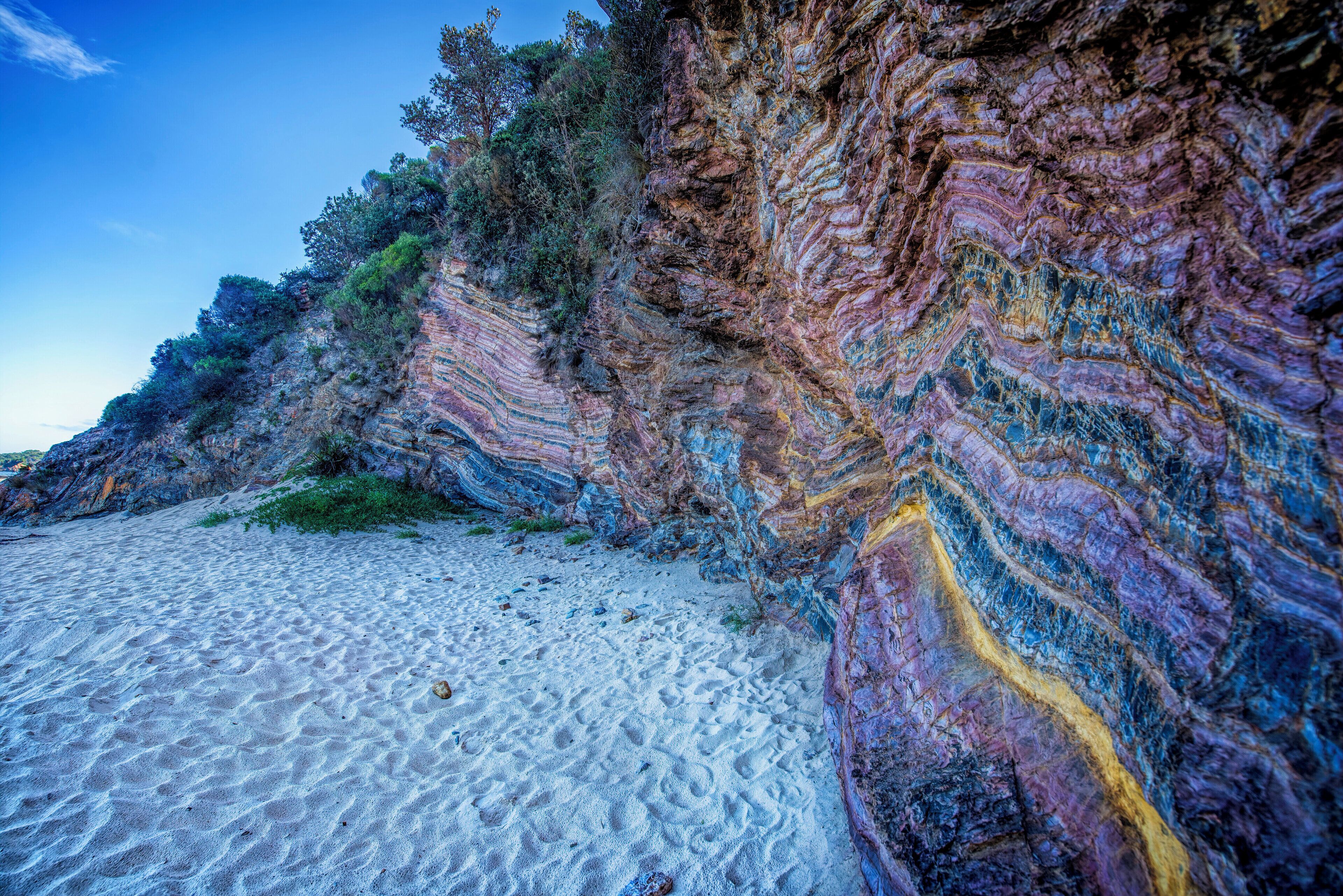 A beach with white sand and colorful rock formations.