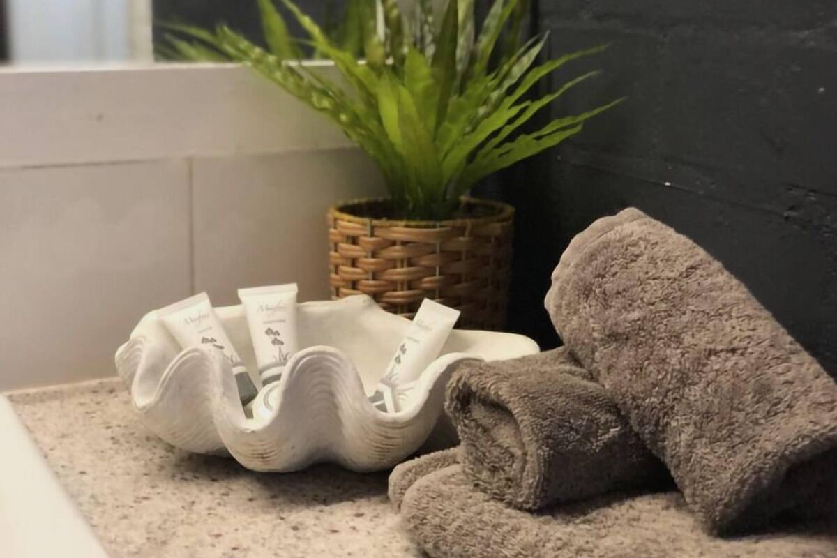 A bathroom with a woven basket containing toiletries, a rolled towel, and a potted plant.