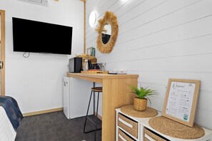 A modern kitchen area with a flat-screen TV, a refrigerator, a coffee machine, and a small bar counter. - Mallacoota Hotel Motel (Mallacoota)