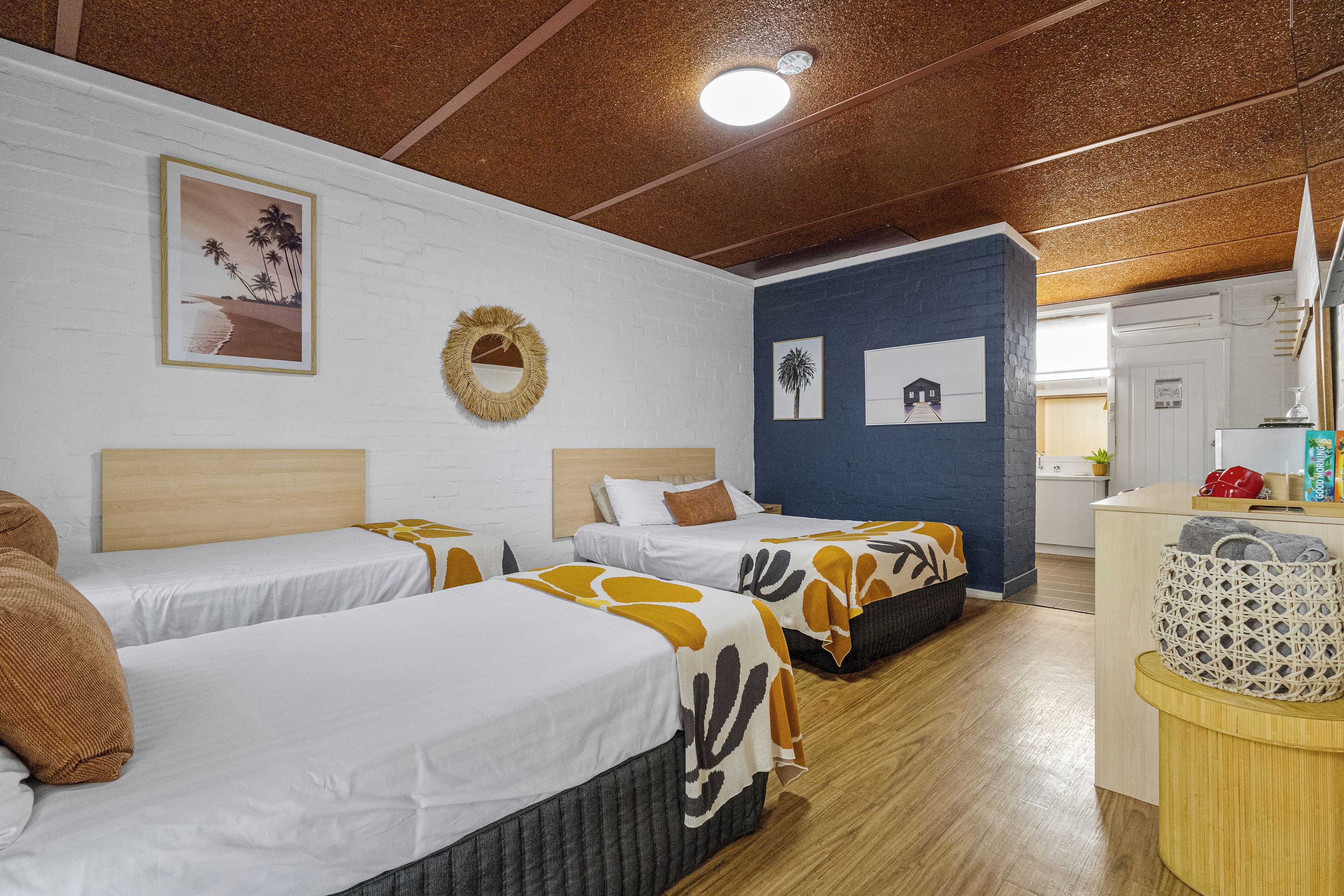 A hotel room with two beds, a wooden ceiling, a white brick wall, and a blue accent wall.