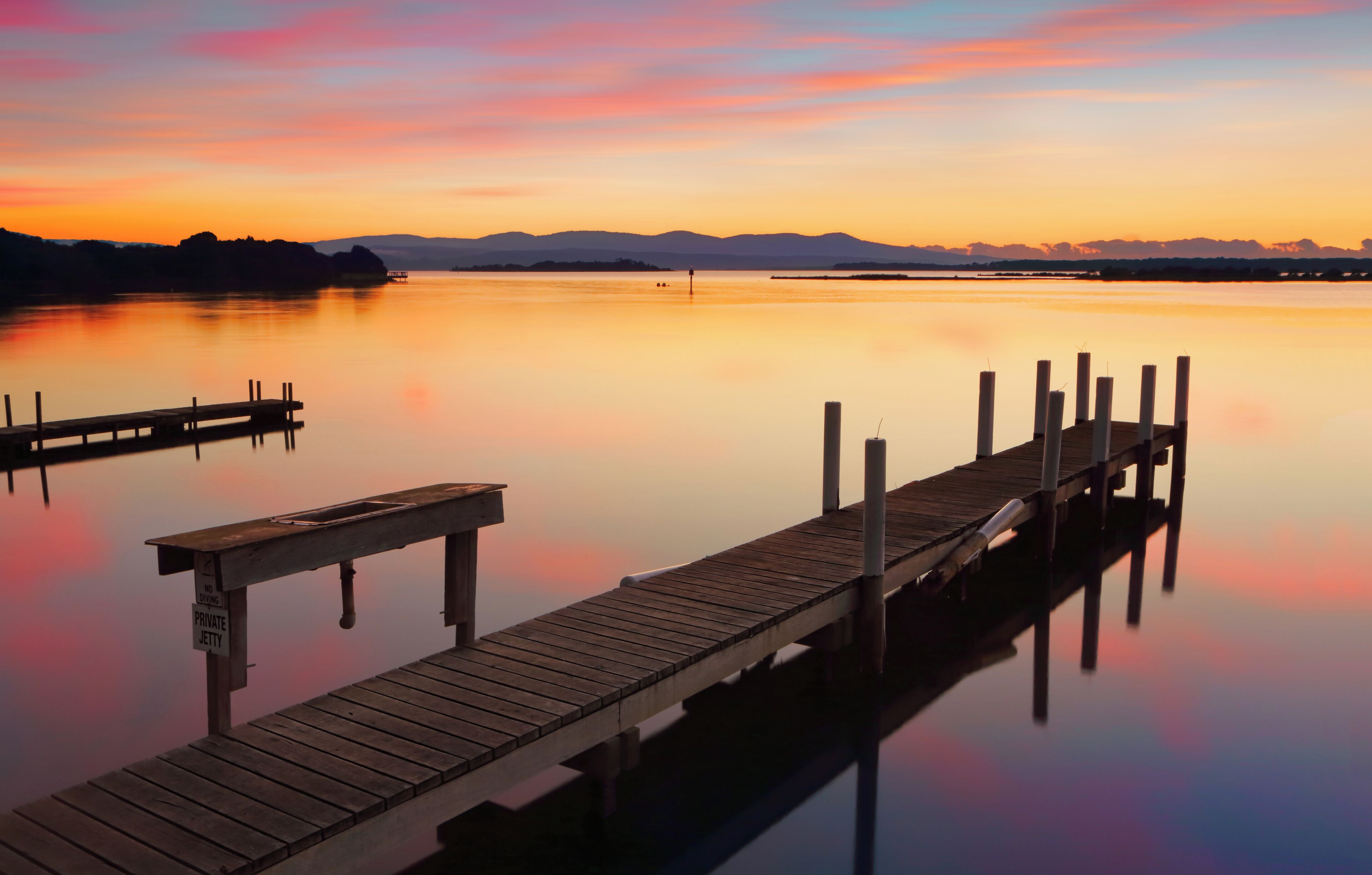 A wooden pier extending into calm water with a sunset in the background.