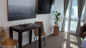 A hotel room with a large window, a flat-screen TV mounted on the wall, a dining table with chairs, a potted plant, and a bed with a patterned bedspread. - Mallacoota Hotel Motel (Mallacoota)