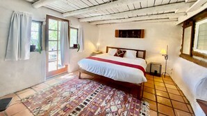 A bedroom with a bed, a window, a door, a rug, and a ceiling with wooden beams.